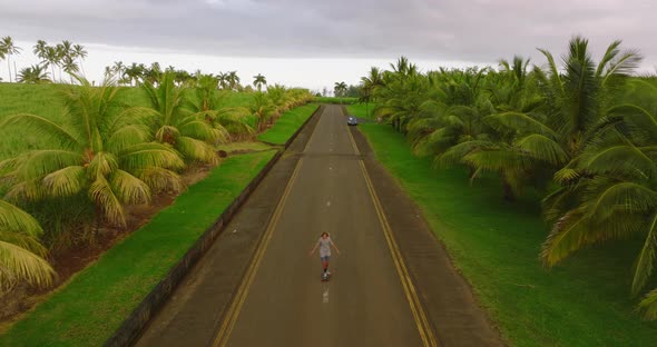 A Teenager Rides a Longboard Along a Beautiful Road with Green Palm Trees