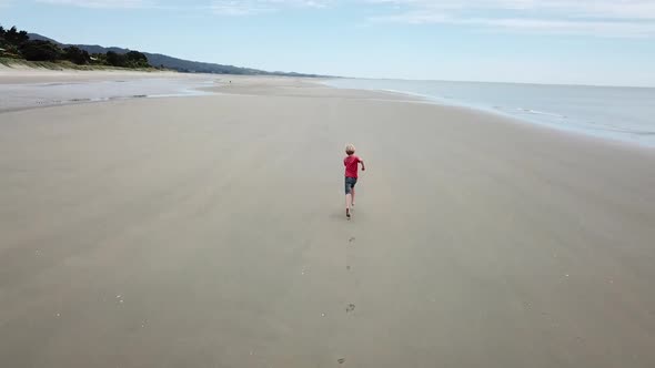 AERIAL FOLLOWING shot of a boy running along a beach
