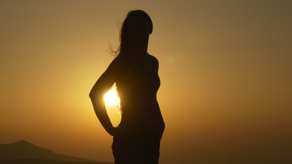 Woman Stands At Sunset In Backlighting