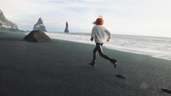 Yong Redhaired Woman Traveler Running on Volcanic Black Sand Beach in Iceland