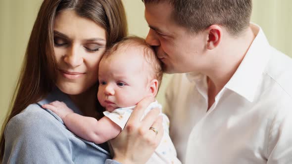 Mom and Dad Hold in Their Arms and Kiss the Infant