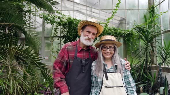Smiling Attractive Retired Couple which Looking at Camera in Beautiful Greenhouse