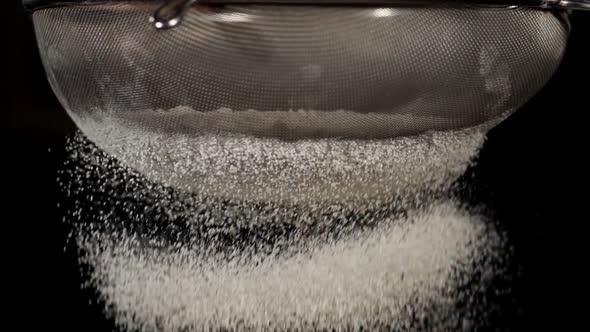 Closeup of White Flour is Falling Through a Steel Sieve on Black Background