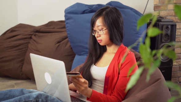 Young Asian Woman Buy Online On The Computer Sitting On The Bean Bag Chair. alt