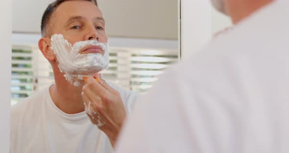 Man shaving his beard with razor in bathroom 