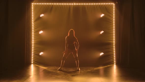 Silhouette of a Sporty Slender Woman in Black Underwear Dancing Twerk in a Dark Studio with Bright