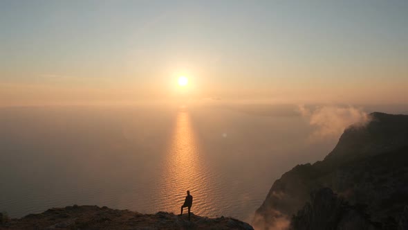 Aerial Shot of the Silhouette of an Active Tourist Standing on the Edge of a High Mountain Above the