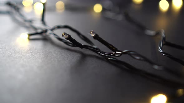 Christmas garland with yellow lights and a black wire on a dark background. 