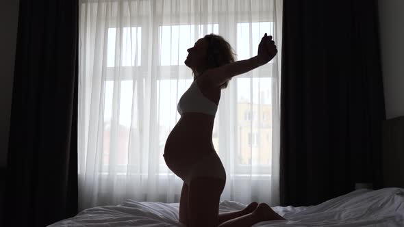 Pregnancy And Good Morning Concept, Silhouette Of Pregnant Woman Stretching And Waking Up On Bed