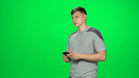 Smiling Man Goes and Texting with Smartphone on Green Screen at Studio.