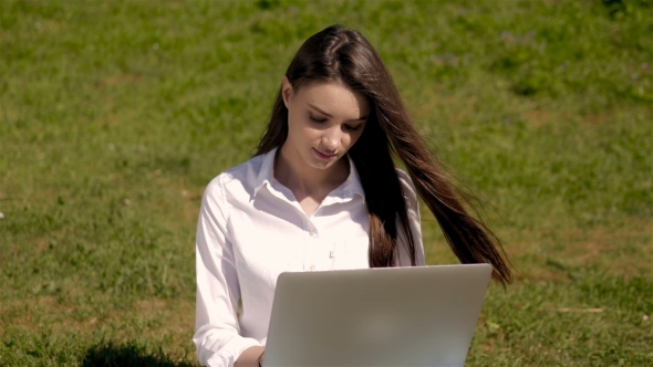 Portrait Of Cute Student Girl Working With Laptop In Park Of a University Campus