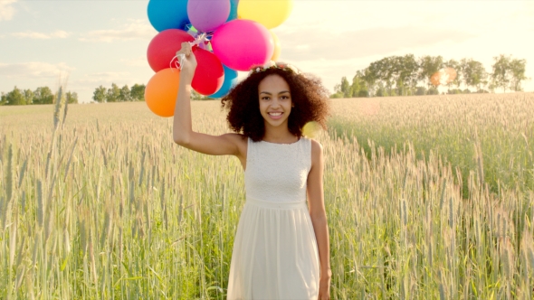 Young Girl Walking Through a Wheat Field With Colour Balloons During Sunset