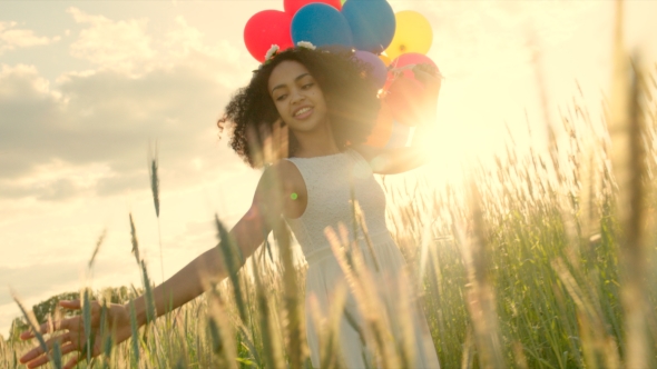 Young Girl Walking Through a Wheat Field With Colour Balloons During Sunset