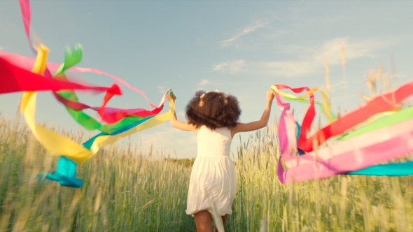 Young Girl Running With Colored Ribbons In Her Hands Through The Wheat Field