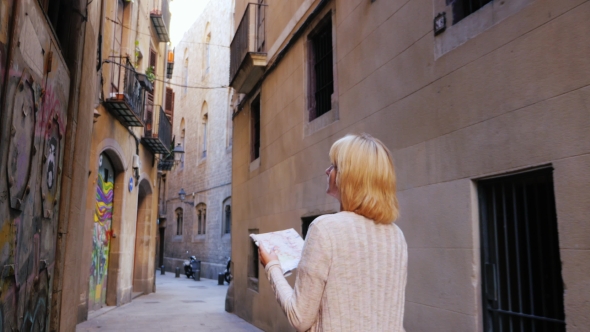 Woman With Map Walking Along The Narrow Street Of The Old City. Tourists Looking For The Road