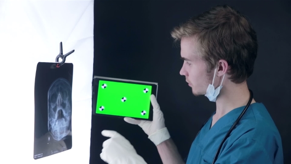 Male Doctor Examining An X-ray Image, Using Green Screen Tablet.