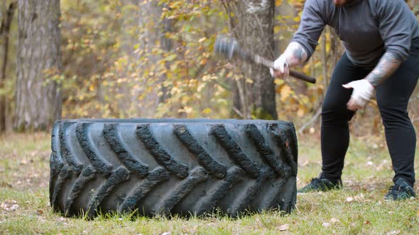 A Big Man Bodybuilder Hitting the Truck Tire with a Hammer - Autumn Forest