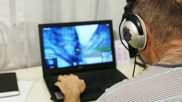 Man Using Laptop Computer At Home. A Man Playing a Computer Game With Headphones