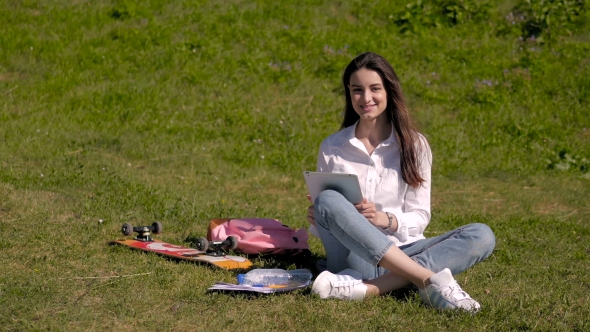 Beautiful Happy Smiling Brunette Using Tablet PC Sitting In Park On a Sunny Day