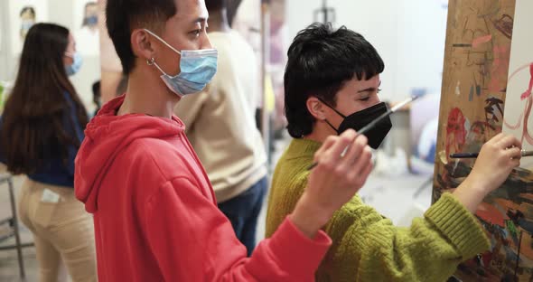 Multiracial students painting inside art room class wearing safety masks