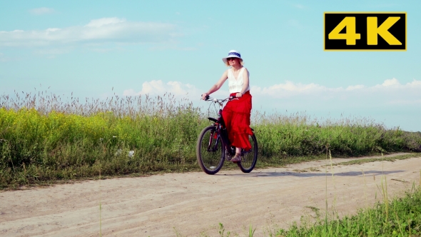 The Lady On The Bike In The White Hat Rides On The Field On a Country Goes To The Camera