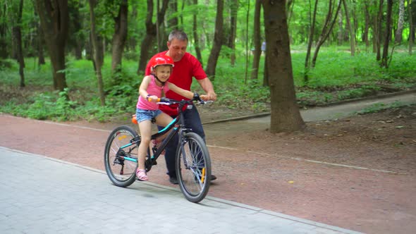 Father teaching daughter to ride bike at urban park. Child girl learning biking with the dad's help.