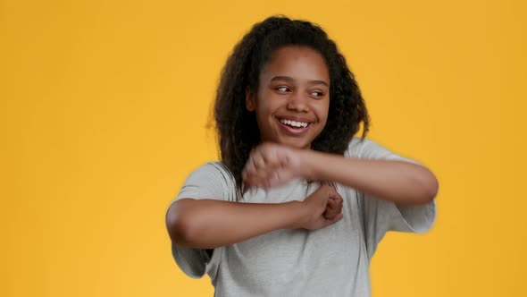 Black Teenager Girl Dancing Making Funny Movements Over Yellow Background