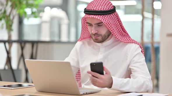 Professional Arab Businessman Using Smartphone and Laptop in Office