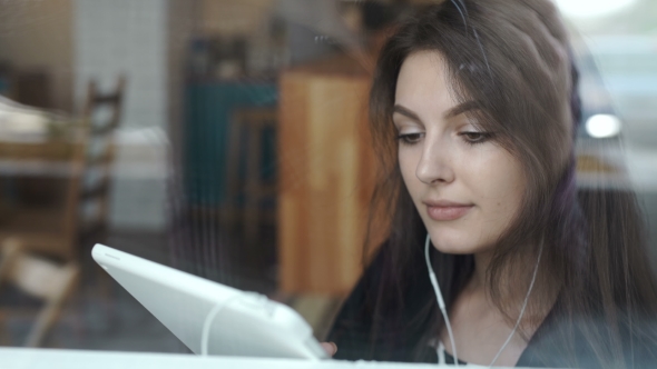 Young Woman Using Tablet In Coffee Shop With Headphone