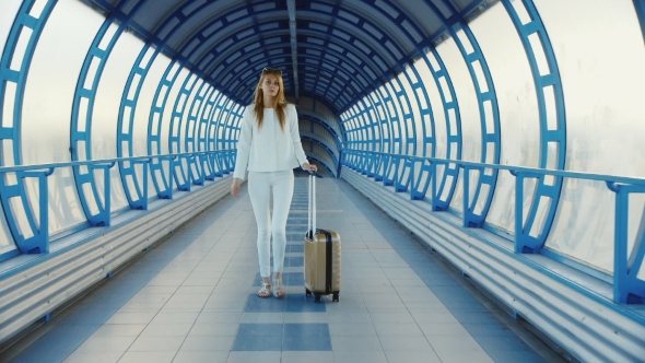 Young Business Woman With Travel Bag On Wheels Is On The Transition From The Terminal At The Airport