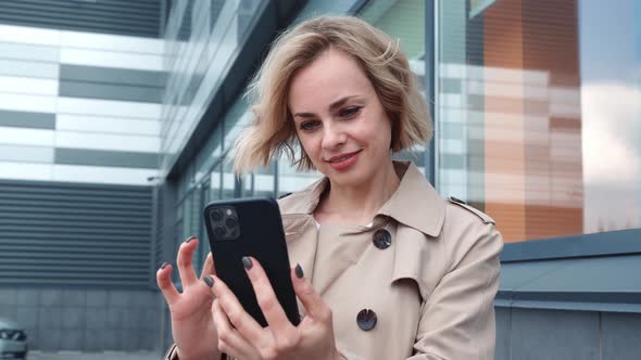 Stylish Business Woman in Raincoat Using Smartphone