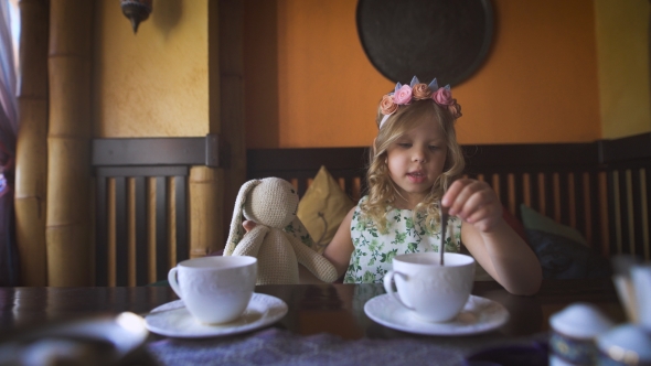 A Little Girl Is Having Tea With Her Stuffed Rabbit In a Cozy Cafe.