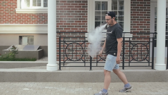 Young Man Walking On The Street And Smoke E-Cigarette. Vape. 