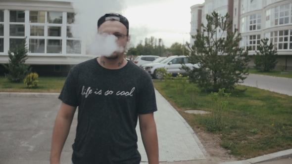 Young Man Walking On The Street And Smoke E-Cigarette. Vape. 