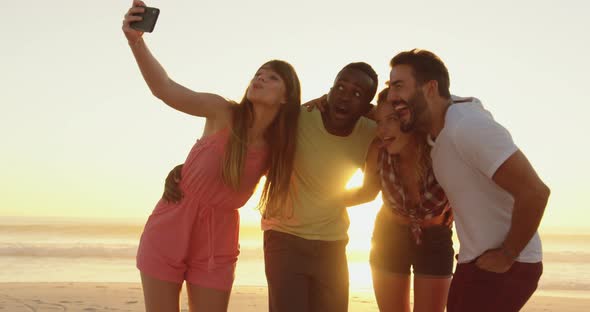 Young adult friends taking seflies on the beach at sunset 4k