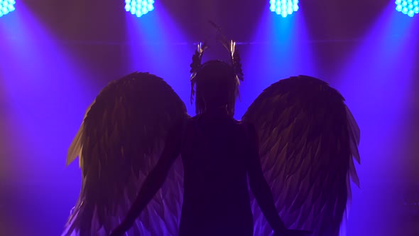 Silhouette of Dancing Greek Goddess Artemis with Wings on Stage in a Dark Studio with Smoke and Neon