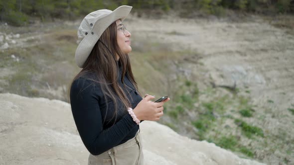 Girl in Hat Uses Phone and Smiles at Camera in Stony Landscape Close