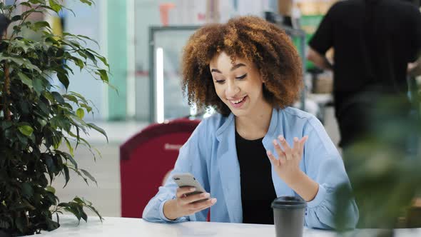 Young Beautiful Girl Teenager Millennial African American Woman with Curly Hair Sits in Cafe Looking