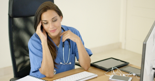 Healthcare Worker Wearing Scrubs Sits At Computer