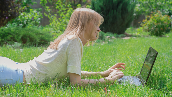 Beautiful Girl Using Notebook Laying on Grass in Park 1