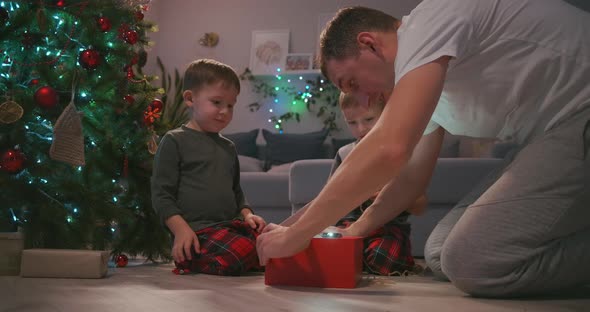 Father with Two Children Opens a Christmas Present Under the Tree and Rejoices