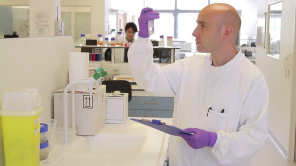 Male scientist looking at tube and making notes in Laboratory