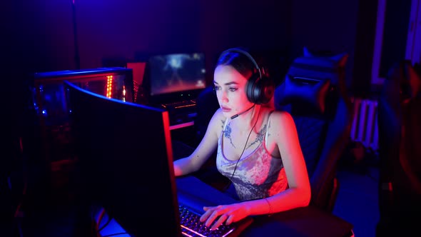 Gaming Concept - Young Sexy Woman with Tattoos Sits in the Chair in Neon Gaming Club and Playing an