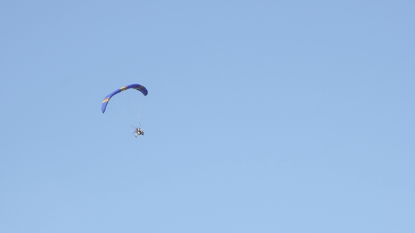 Parachute With Motor Flying On Blue Cloudy Sky