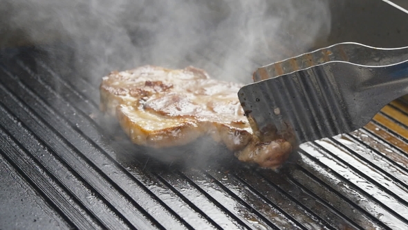 A Cook Turns Up a Steak Of Meat On a Grill In 