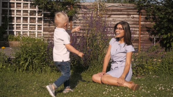 Little Boy Brings Flower To His Mom. Happy Young Family Having Fun Outdoors. Mom And Kid Enjoying