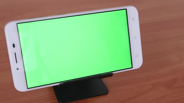 Slide motion of The green screen phone is placed on a pedestal on a wooden table.