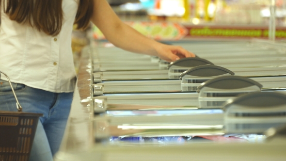 Young woman taking product from fridge in shop and putting it into the basket