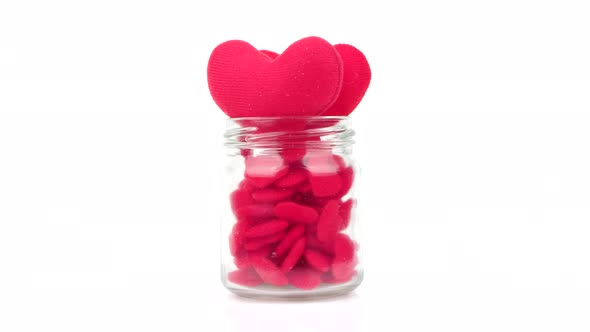 Rotation Small red heart on a clear glass jar isolated on white background.