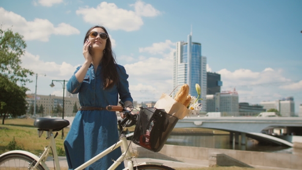 Beautiful Girl Standing in the Street With a Bike With Basket Talking on the Phone and Smiling